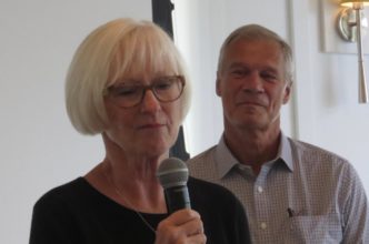 Woman speaking into microphone, man standing behind